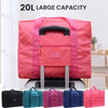 A pink foldable travel duffel bag with a black handle and luggage strap is displayed on a wooden surface.