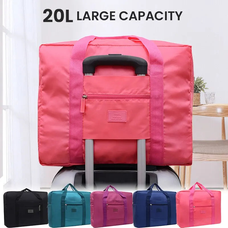 A pink foldable travel duffel bag with a black handle and luggage strap is displayed on a wooden surface.