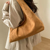 A tan suede shoulder tote bag carried by a person wearing a light colored shirt.