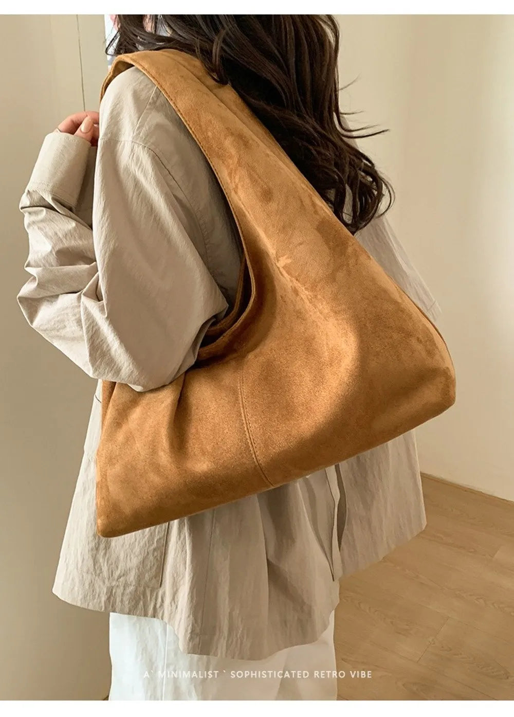A tan suede shoulder tote bag carried by a person wearing a light colored shirt.