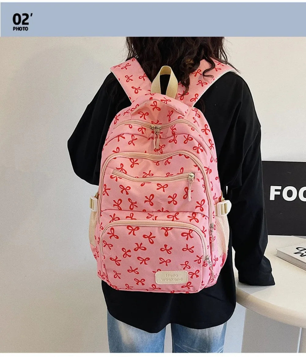 A pink nylon backpack with a cute bow print is worn by a person against a white background.