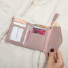 A light pink PU leather coin clutch wallet with various cards and a tassel resting on a cream fabric.