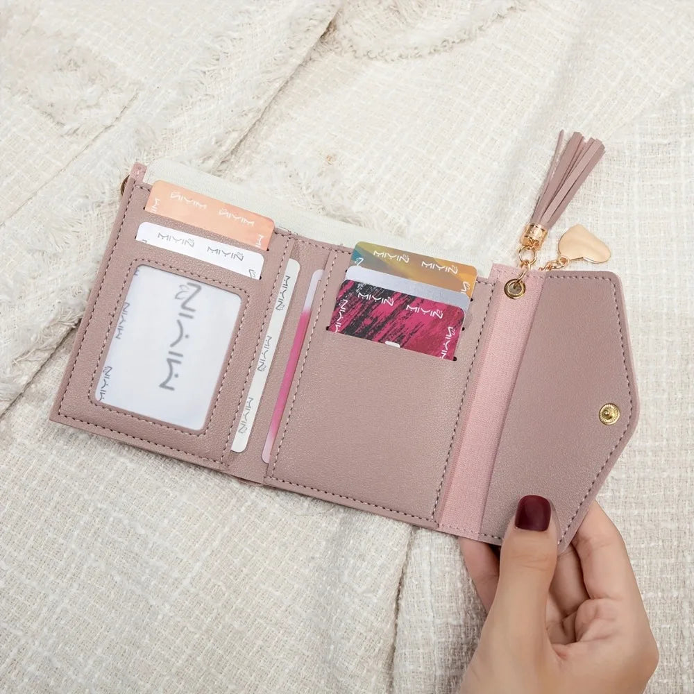 A light pink PU leather coin clutch wallet with various cards and a tassel resting on a cream fabric.