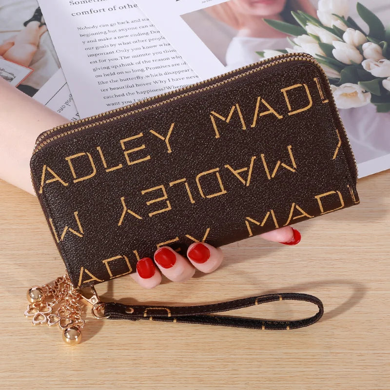 Cartera con cremallera de imitación de cuero marrón oscuro y herrajes dorados sobre una superficie de madera.