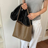 A person holds a brown woven bucket bag and a black leather garment against a white door frame.