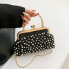 A black pearl embellished crossbody shoulder bag with gold hardware being held by a hand.