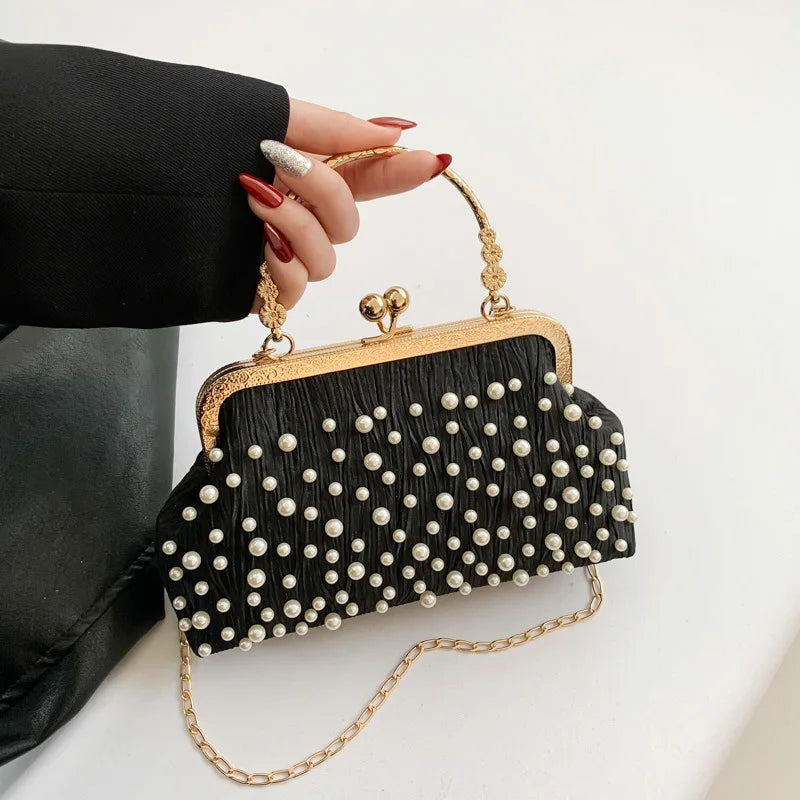 A black pearl embellished crossbody shoulder bag with gold hardware being held by a hand.