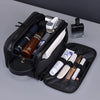 A black PU leather travel toiletry bag with organizer pockets and various grooming tools is shown on a gray surface.