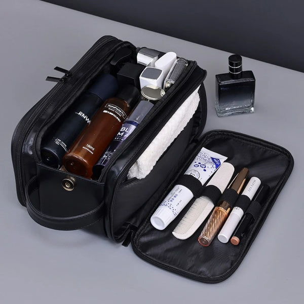 A black PU leather travel toiletry bag with organizer pockets and various grooming tools is shown on a gray surface.