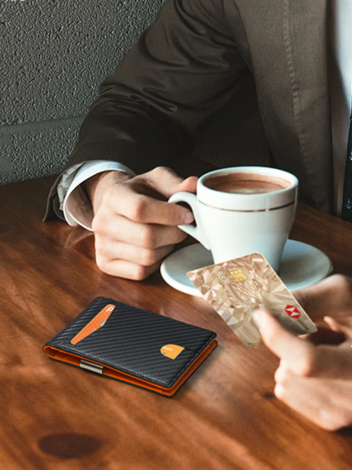 A hand holds a brown coffee cup and a clear RFID-blocking wallet on a wooden table.