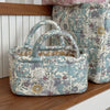 A quilted fabric storage basket in soft blue and cream floral patterns sits on a wooden shelf.