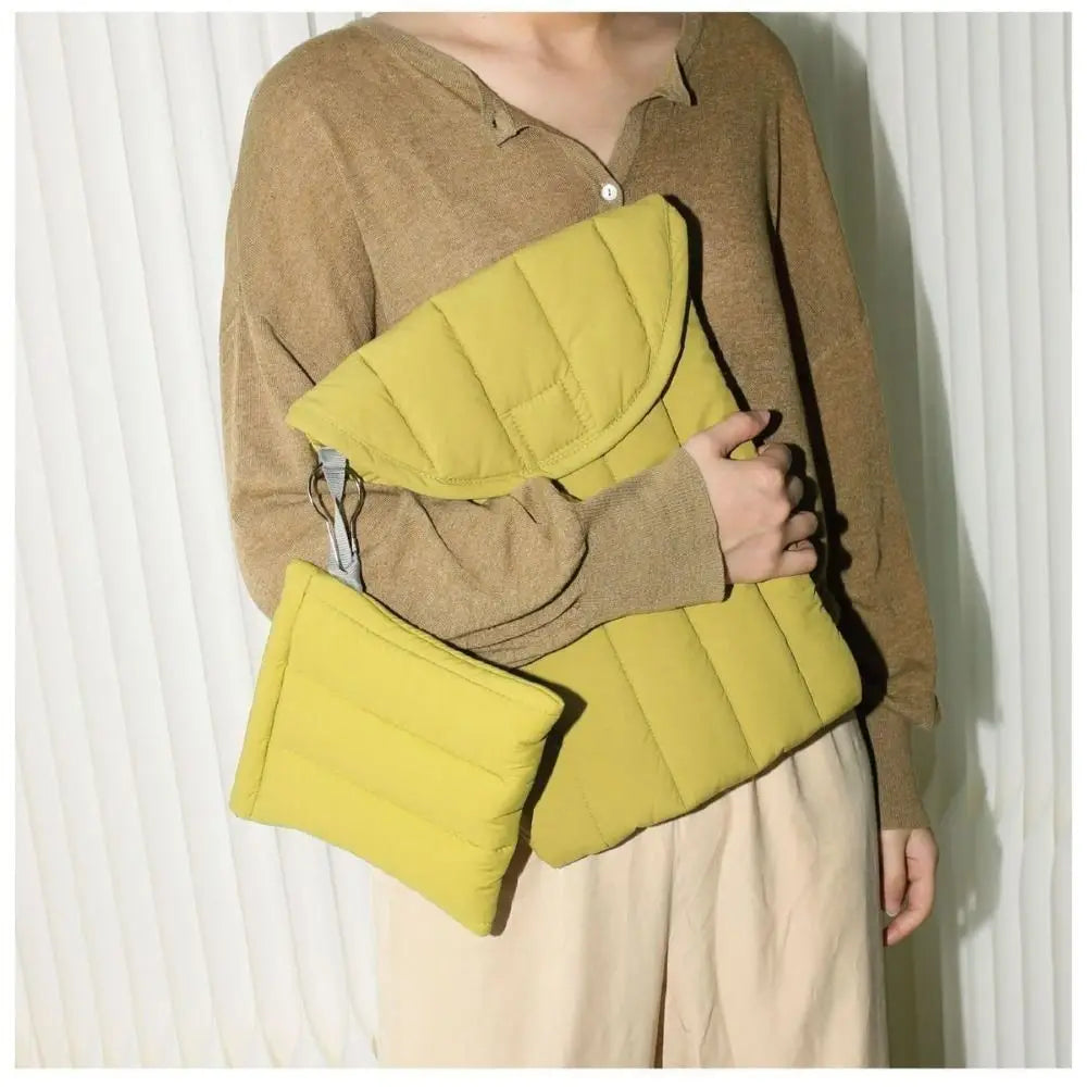 A person is holding a yellow quilted laptop sleeve against a brown sweater and beige pants.