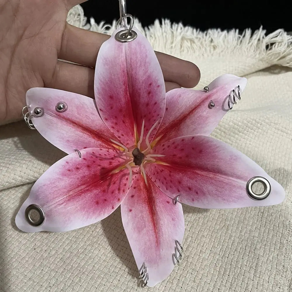 A realistic pink and red orchid flower keychain is held in a hand against a white background.