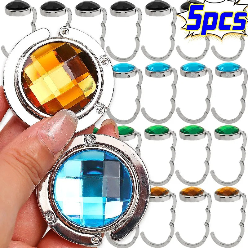 A hand holds a round acrylic foldable hook for bags and keys, showing its design and function.