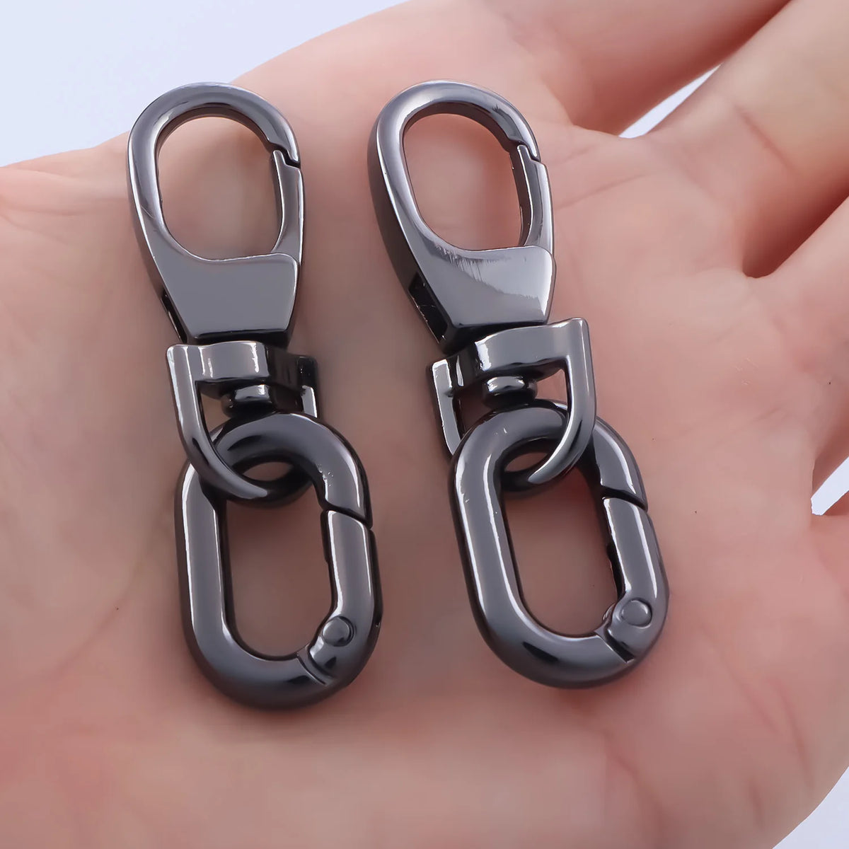 A pair of silver metal swivel lobster claw clasps with key rings resting on a person's hand.