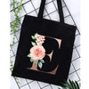 Black canvas tote bag featuring a large gold letter C design with pink floral accents.