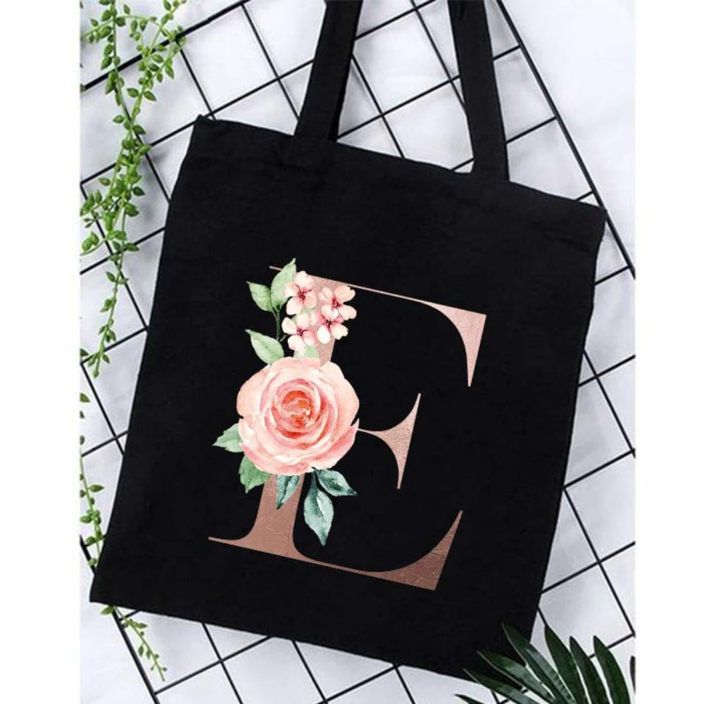 Black canvas tote bag featuring a large gold letter C design with pink floral accents.