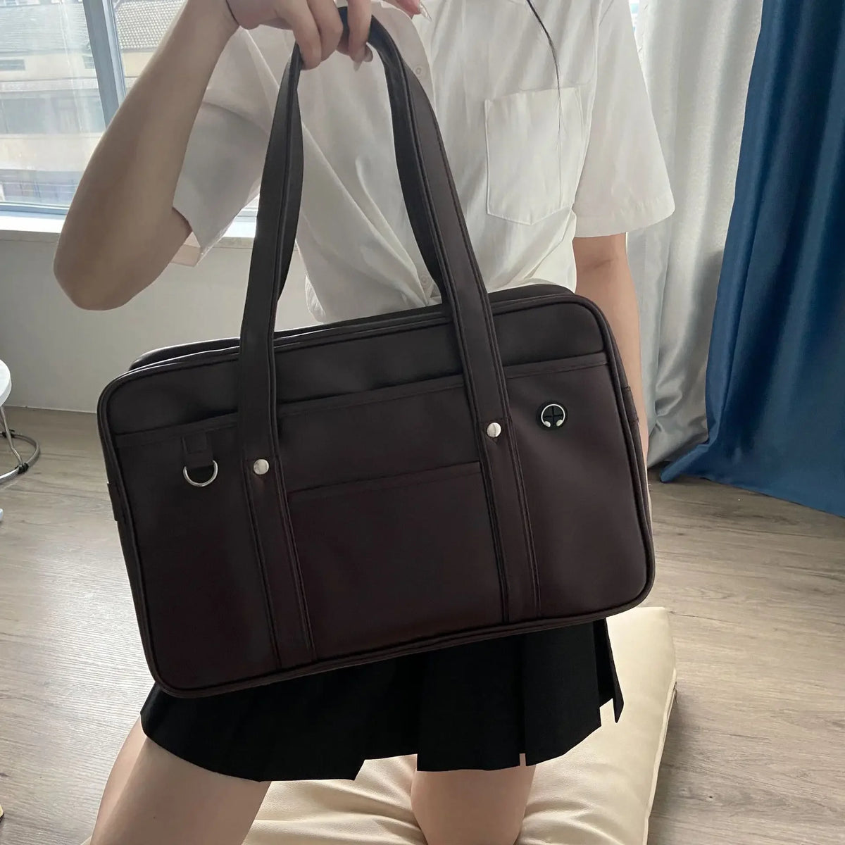 A person is holding a dark brown Japanese style student messenger bag made of waterproof PU leather.