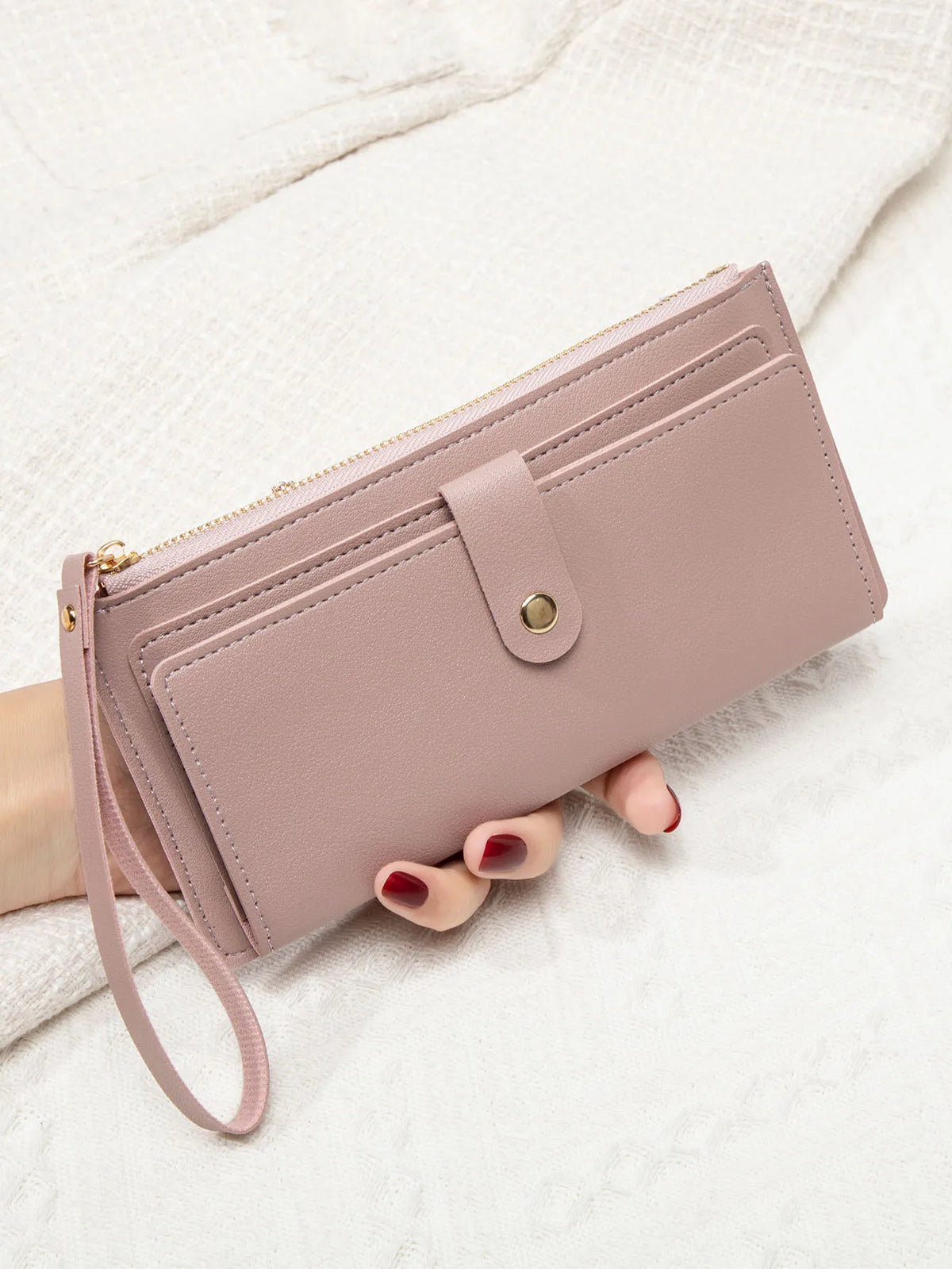 A mauve PU leather coin purse and card holder is held by a hand against a white textured background.