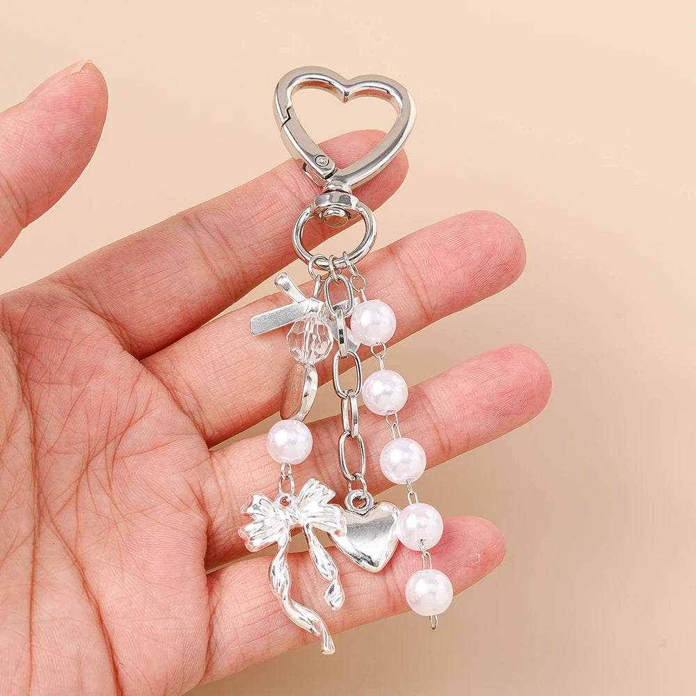 Silver pearl bow heart keychain hanging from a split ring on a hand