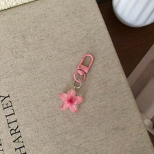 A pink resin flower keychain with a silver ring attached, resting on a beige fabric surface.