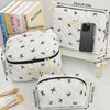 A white quilted makeup bag with black trim and a gold drawstring is shown next to various cosmetic brushes.