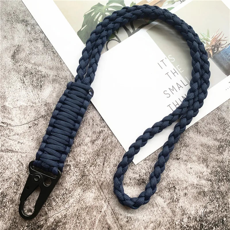 A dark blue hand-woven nylon lanyard with a metal hook is displayed on a textured surface.