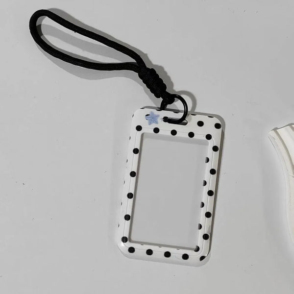 A white card holder with a rectangular frame and black polka dots is attached to a black lanyard.