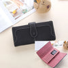 A black leather clutch wallet is shown next to a pink leather wallet on a light surface.