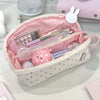 A pink polka dot shell pencil case filled with various stationery items and a white bunny charm.