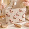 A beige cosmetic bag with a repeating pattern of pink and brown dachshunds rests on a light surface.