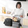 A woman holds an insulated thermal lunch bag containing a meal on a kitchen counter.