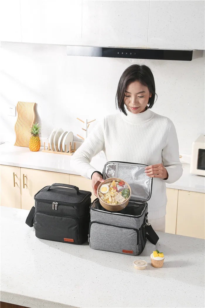 A woman holds an insulated thermal lunch bag containing a meal on a kitchen counter.