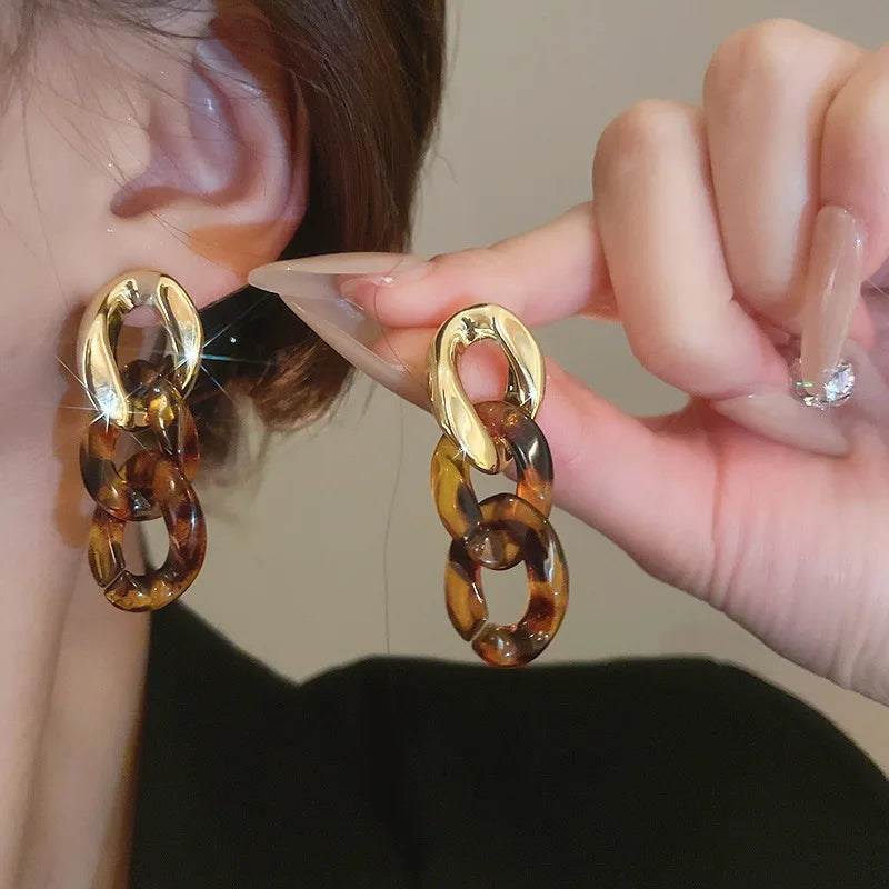 Gold-toned interlocking leopard print dangle earrings held by a hand