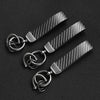 A black carbon fiber leather keychain with silver hardware lying on a dark surface.
