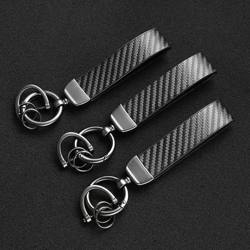 A black carbon fiber leather keychain with silver hardware lying on a dark surface.