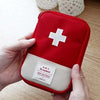 A red pouch for a compact survival and first aid kit with a white cross emblem is held by a hand.
