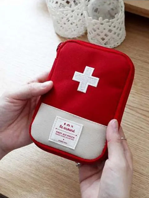 A red pouch for a compact survival and first aid kit with a white cross emblem is held by a hand.