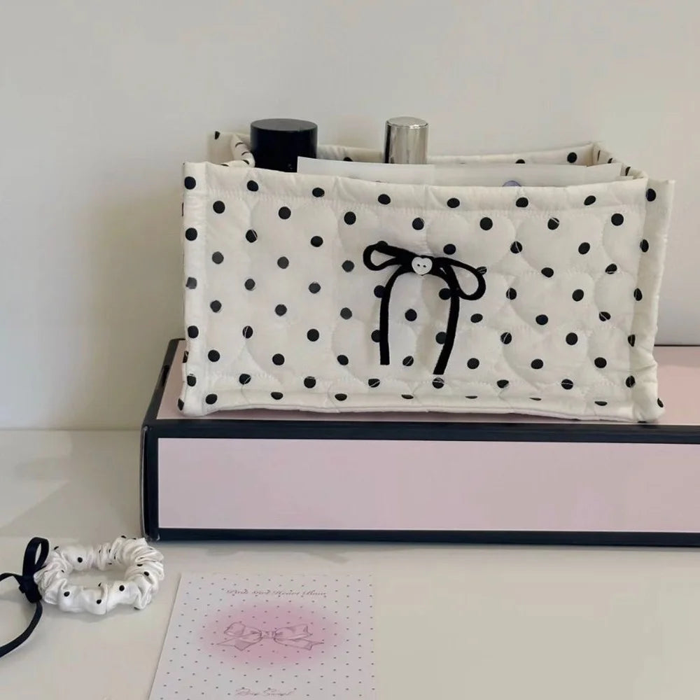 A white quilted cotton storage basket with black polka dots and a black lace flower design resting on a pink box.