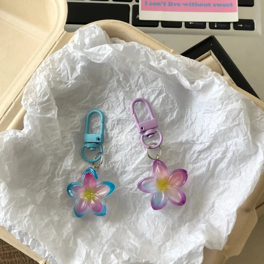 Two colorful resin flower keychains, one blue and one purple, are displayed on white tissue paper.