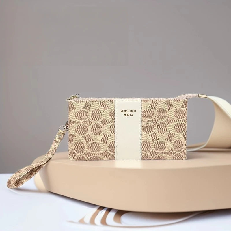 A beige printed faux leather mini crossbody bag with gold hardware resting on a light pink surface.
