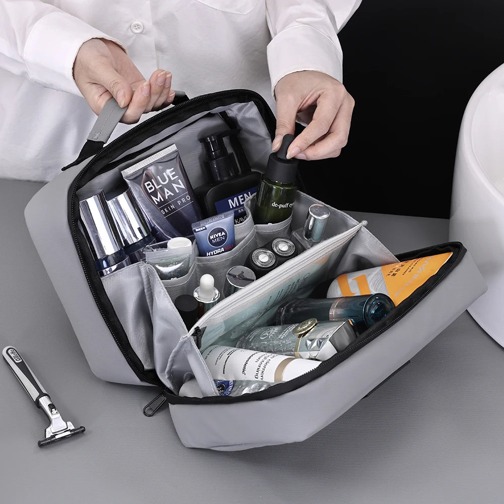 A hand is opening a gray portable waterproof travel toiletry bag filled with various grooming products.