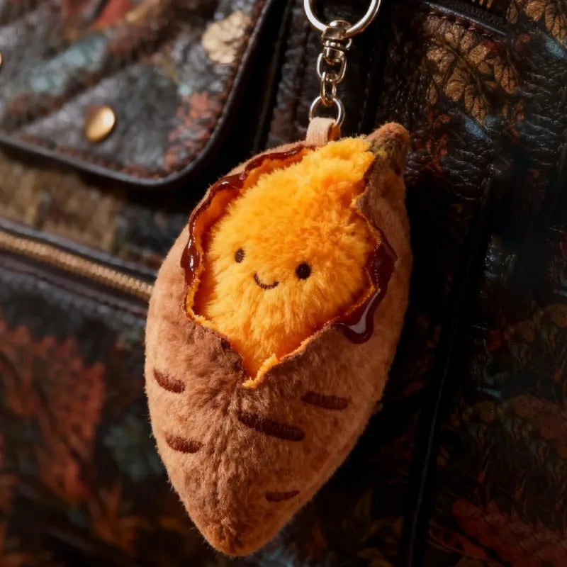 A small, round plush keychain shaped like a roasted sweet potato with orange and yellow fluff.