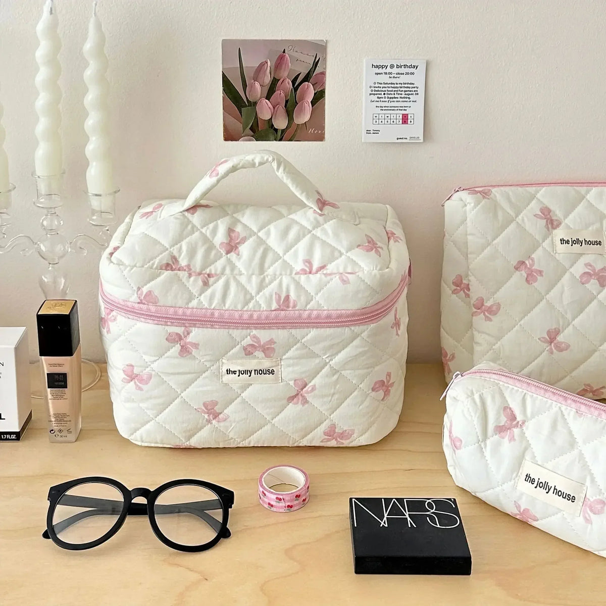 Sac de rangement cosmétique blanc avec motif nœud rose, exposé sur une surface en bois à côté de lunettes et d'un calendrier.
