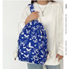 A woman is holding a blue butterfly patterned backpack against a white shirt.