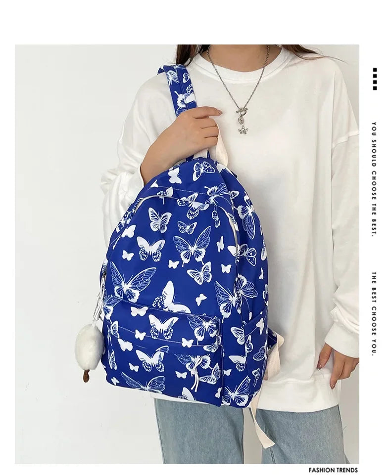 A woman is holding a blue butterfly patterned backpack against a white shirt.