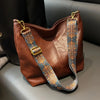 A brown leather geometric strap crossbody hobo bag with a patterned blue and gold strap.