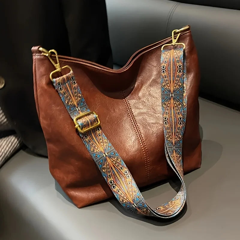 A brown leather geometric strap crossbody hobo bag with a patterned blue and gold strap.