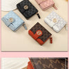 A collection of five compact wallets in various colors and patterns, including pink, black, blue, and beige, displayed on a l