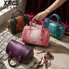 A collection of luxury crocodile pattern crossbody tote bags in various shades of green, pink, and purple displayed on a wood
